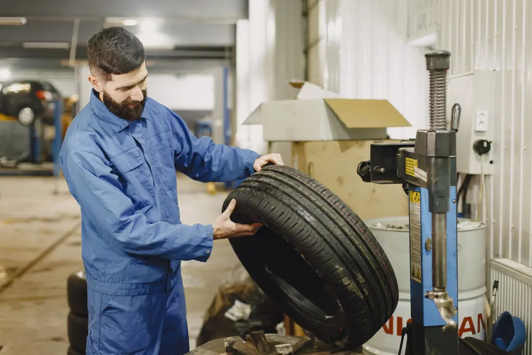 Mecânico em macacão azul posicionando pneu em máquina de balanceamento em oficina automotiva